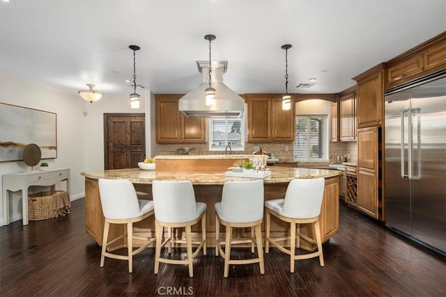 kitchen featuring a large island, dark hardwood / wood-style floors, stainless steel built in refrigerator, and decorative light fixtures