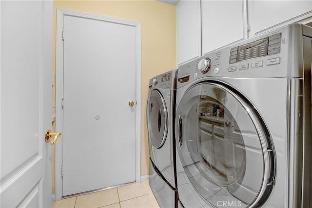 clothes washing area with washer and dryer, cabinets, and light tile patterned floors