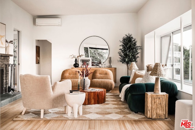 living area with a wall mounted air conditioner, hardwood / wood-style flooring, and a tiled fireplace