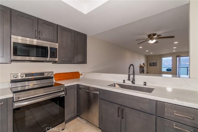 kitchen featuring light stone countertops, appliances with stainless steel finishes, ceiling fan, sink, and light tile patterned floors