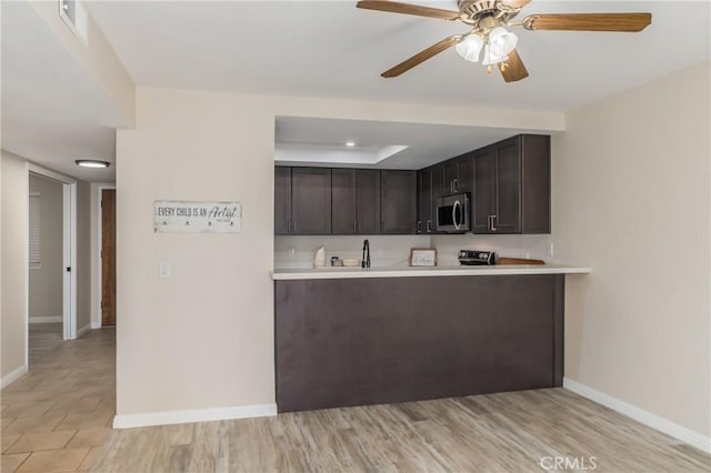 kitchen with kitchen peninsula, ceiling fan, dark brown cabinets, and light hardwood / wood-style flooring