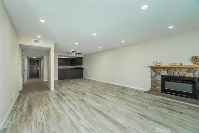 unfurnished living room featuring a stone fireplace, ceiling fan, and hardwood / wood-style floors