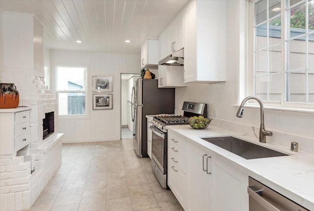 kitchen featuring light stone countertops, appliances with stainless steel finishes, white cabinetry, a healthy amount of sunlight, and sink