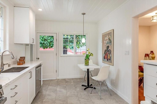 kitchen featuring light stone countertops, white cabinetry, sink, hanging light fixtures, and stainless steel dishwasher