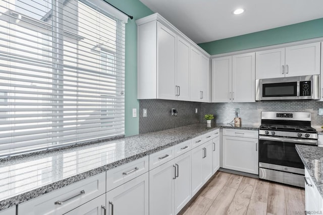 kitchen with light stone countertops, white cabinetry, appliances with stainless steel finishes, and light wood-type flooring