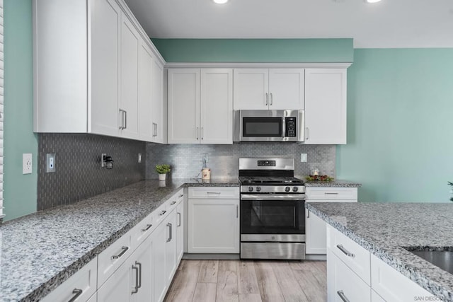 kitchen with white cabinetry, stainless steel appliances, tasteful backsplash, light stone countertops, and light wood-type flooring