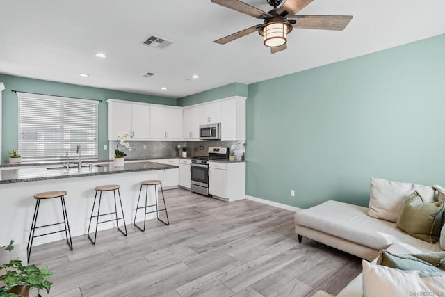 kitchen featuring appliances with stainless steel finishes, a breakfast bar, sink, white cabinets, and dark stone counters