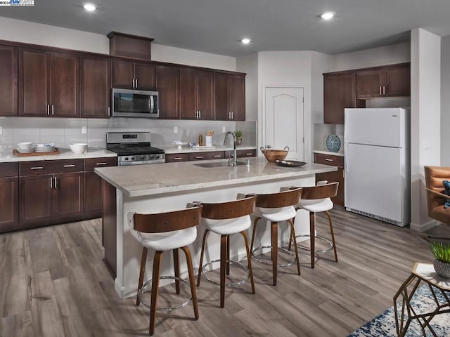 kitchen featuring appliances with stainless steel finishes, light wood-type flooring, tasteful backsplash, sink, and an island with sink