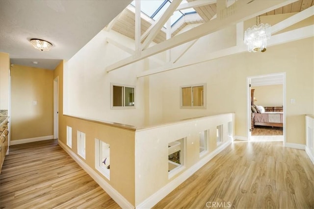 corridor featuring a skylight, high vaulted ceiling, beamed ceiling, a chandelier, and light hardwood / wood-style floors