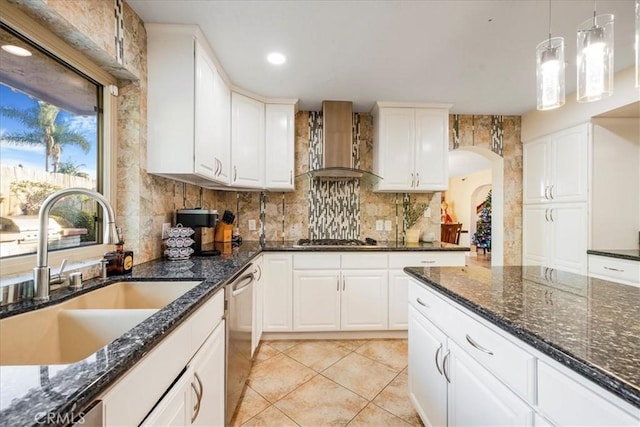 kitchen featuring dark stone counters, wall chimney exhaust hood, stainless steel appliances, sink, and white cabinets