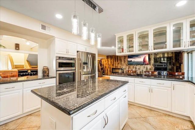 kitchen featuring decorative backsplash, appliances with stainless steel finishes, dark stone counters, a center island, and white cabinetry