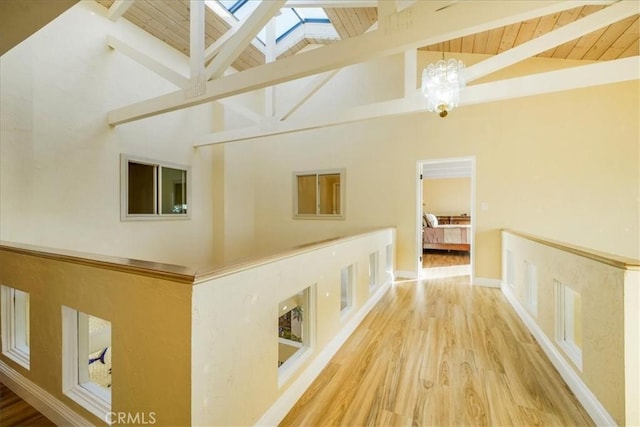 corridor featuring a skylight, wood-type flooring, high vaulted ceiling, wooden ceiling, and beamed ceiling