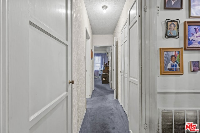 hall featuring dark colored carpet and a textured ceiling