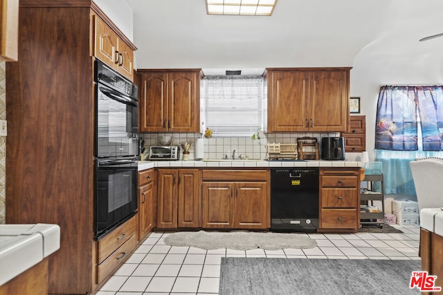 kitchen with black appliances, decorative backsplash, light tile patterned floors, and tile counters