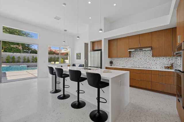 kitchen featuring tasteful backsplash, a kitchen breakfast bar, stainless steel fridge, a towering ceiling, and a kitchen island with sink