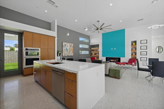 kitchen with ceiling fan, sink, hanging light fixtures, a kitchen island with sink, and appliances with stainless steel finishes