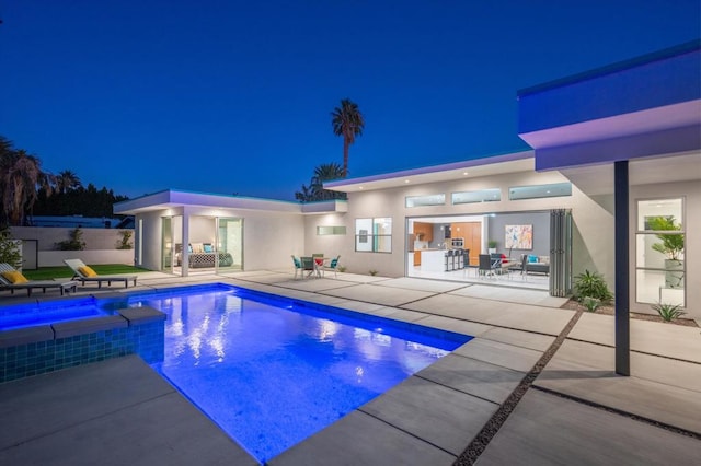 pool at night with an in ground hot tub and a patio