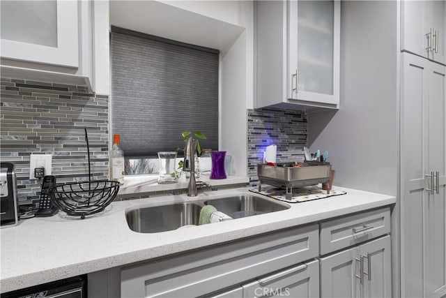 kitchen featuring dishwashing machine, backsplash, light stone countertops, and sink