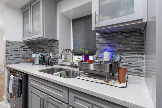 kitchen featuring dishwashing machine, decorative backsplash, sink, light stone counters, and gray cabinetry