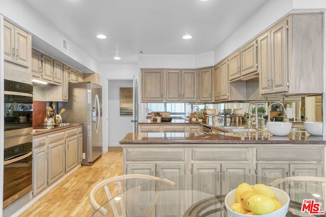 kitchen featuring dark stone counters, sink, light hardwood / wood-style flooring, appliances with stainless steel finishes, and kitchen peninsula