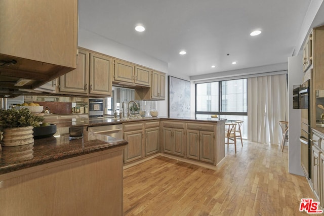 kitchen with sink, dark stone countertops, light wood-type flooring, kitchen peninsula, and stainless steel appliances