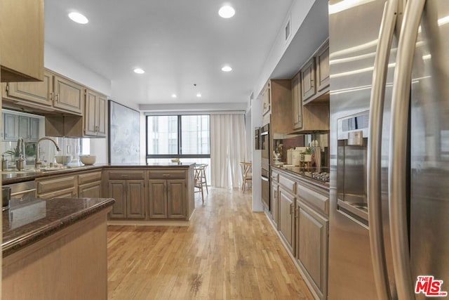 kitchen featuring dark stone counters, sink, stainless steel refrigerator with ice dispenser, light hardwood / wood-style flooring, and kitchen peninsula