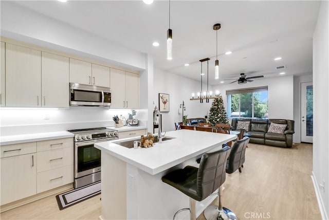 kitchen with decorative light fixtures, light hardwood / wood-style floors, a breakfast bar, sink, and stainless steel appliances