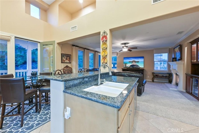 kitchen featuring sink, light tile patterned flooring, dark stone counters, and a center island with sink