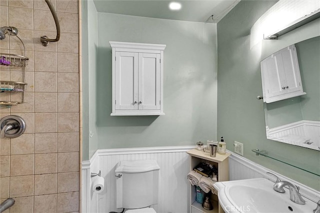 bathroom with toilet, tiled shower, and sink