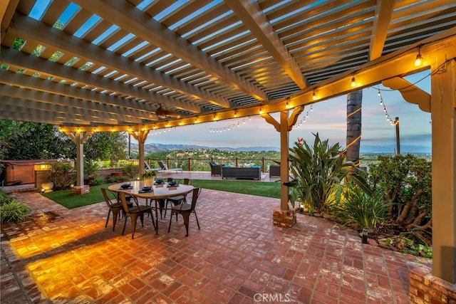 patio terrace at dusk with a mountain view, a pergola, and a hot tub