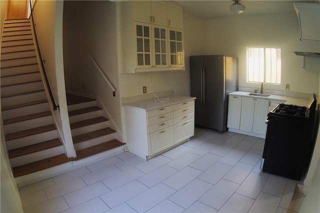 kitchen with sink, light tile patterned floors, black / electric stove, white cabinetry, and stainless steel refrigerator