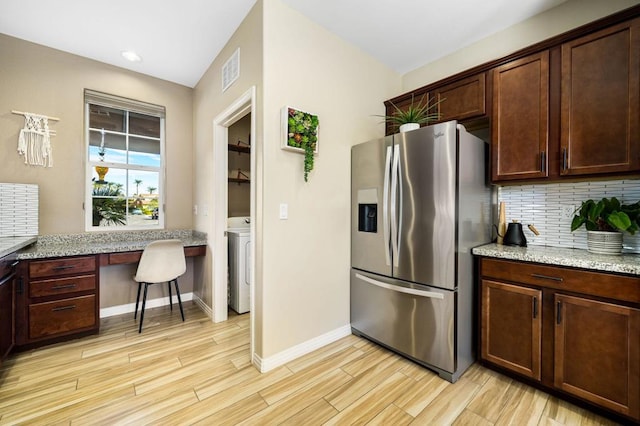 kitchen featuring light stone counters, washer / clothes dryer, stainless steel fridge, built in desk, and light wood-type flooring