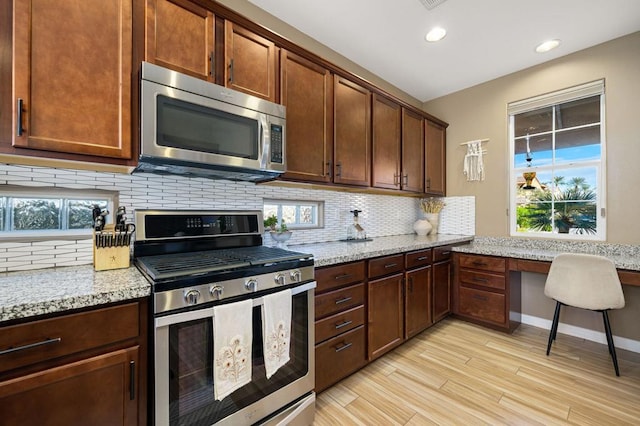 kitchen with stainless steel appliances, light stone counters, backsplash, light hardwood / wood-style floors, and built in desk