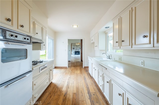 kitchen with white gas stovetop, sink, white cabinets, and light wood-type flooring