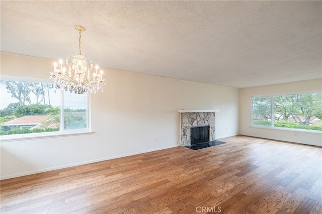 unfurnished living room with a stone fireplace, a chandelier, plenty of natural light, and wood-type flooring