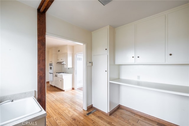 interior space with white cabinets, stainless steel gas stovetop, light wood-type flooring, and sink