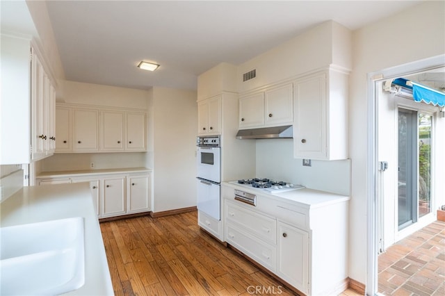 kitchen with white cabinetry, sink, white appliances, and light wood-type flooring