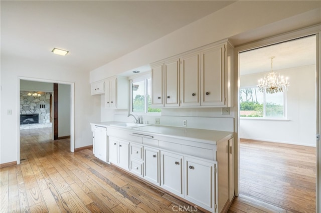 kitchen with white cabinets, light hardwood / wood-style floors, a stone fireplace, and sink