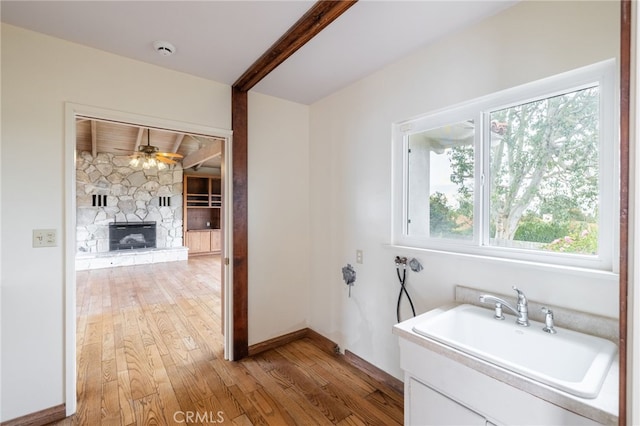 bathroom featuring hardwood / wood-style floors, ceiling fan, a stone fireplace, and sink