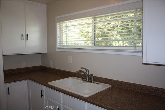 kitchen with dark countertops, white cabinets, and a sink