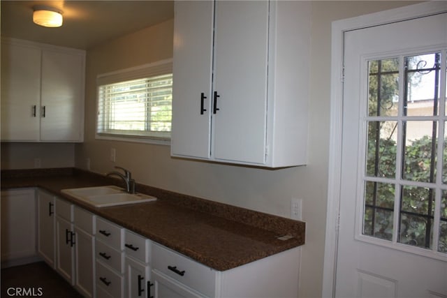 kitchen featuring white cabinets, dark stone countertops, sink, and a wealth of natural light