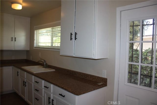 kitchen featuring dark countertops, white cabinetry, and a sink