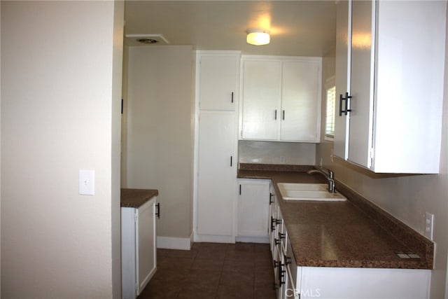 kitchen featuring white cabinetry, sink, dark stone counters, and dark tile patterned flooring