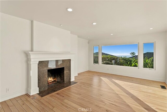 unfurnished living room featuring a premium fireplace and light hardwood / wood-style flooring