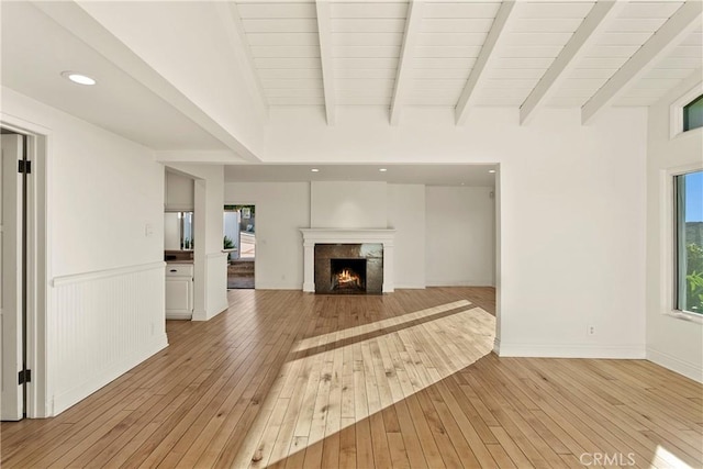 unfurnished living room featuring light hardwood / wood-style flooring, a fireplace, and beamed ceiling