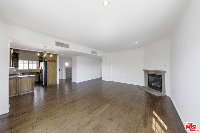 unfurnished living room featuring a notable chandelier, sink, ornamental molding, and dark wood-type flooring