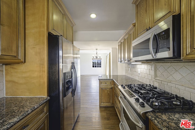 kitchen featuring backsplash, dark stone counters, stainless steel appliances, pendant lighting, and a chandelier