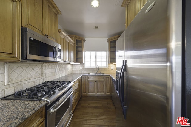 kitchen featuring sink, dark hardwood / wood-style floors, backsplash, dark stone counters, and appliances with stainless steel finishes