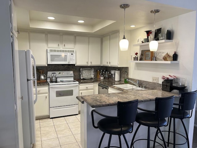 kitchen featuring sink, kitchen peninsula, a tray ceiling, white appliances, and a kitchen bar