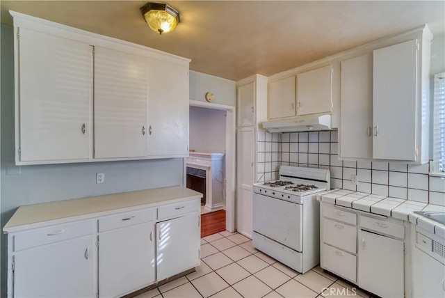 kitchen featuring gas range gas stove, light tile patterned flooring, white cabinets, under cabinet range hood, and tasteful backsplash